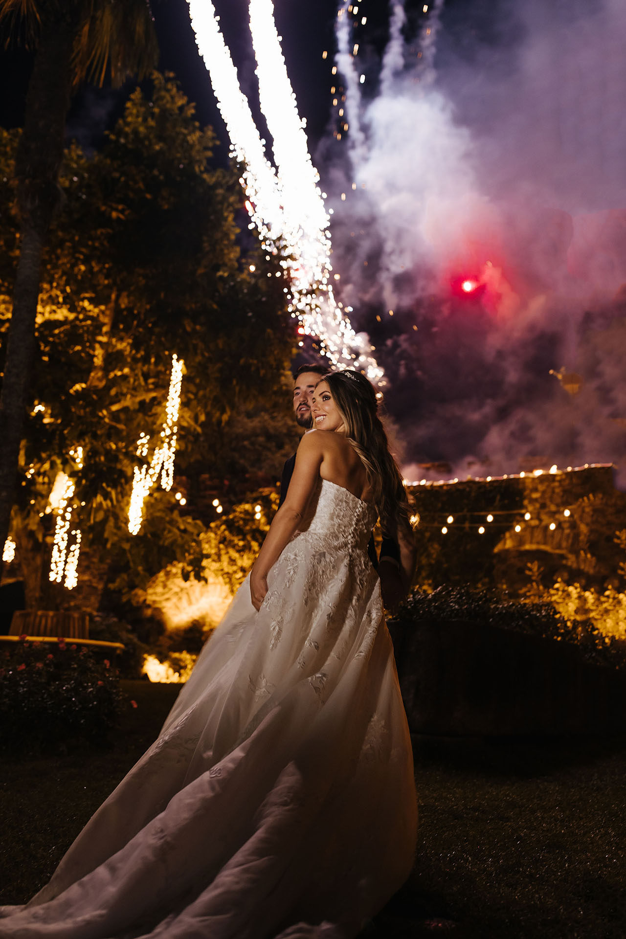 Bride and groom walking together with fireworks in the background at night