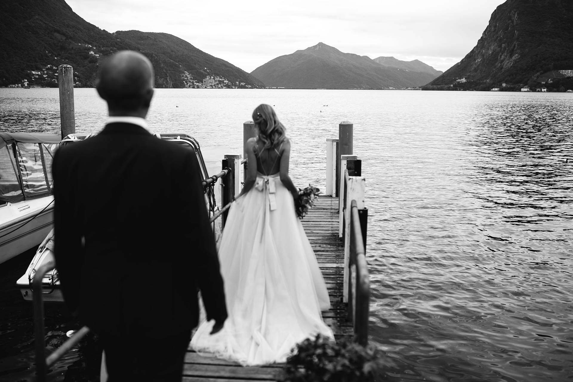 Bride walking along a dock on Lake Lugano with the groom following behind during their wedding day.