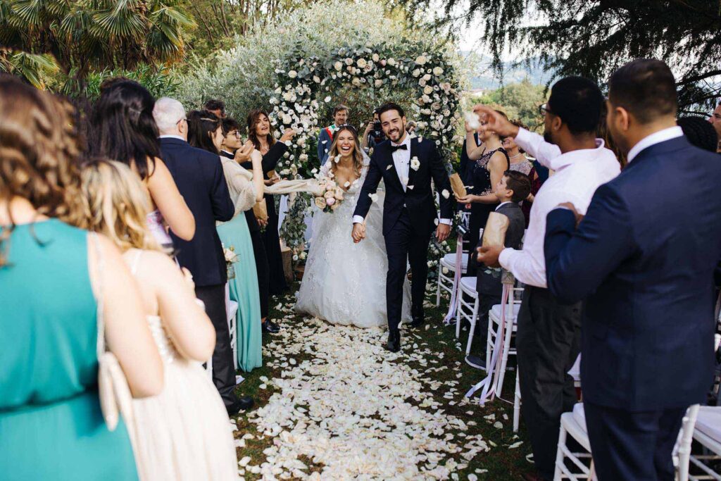 Bride and groom walking down the aisle after ceremony at Castello di Rossino in Italy surrounded by guests throwing petals