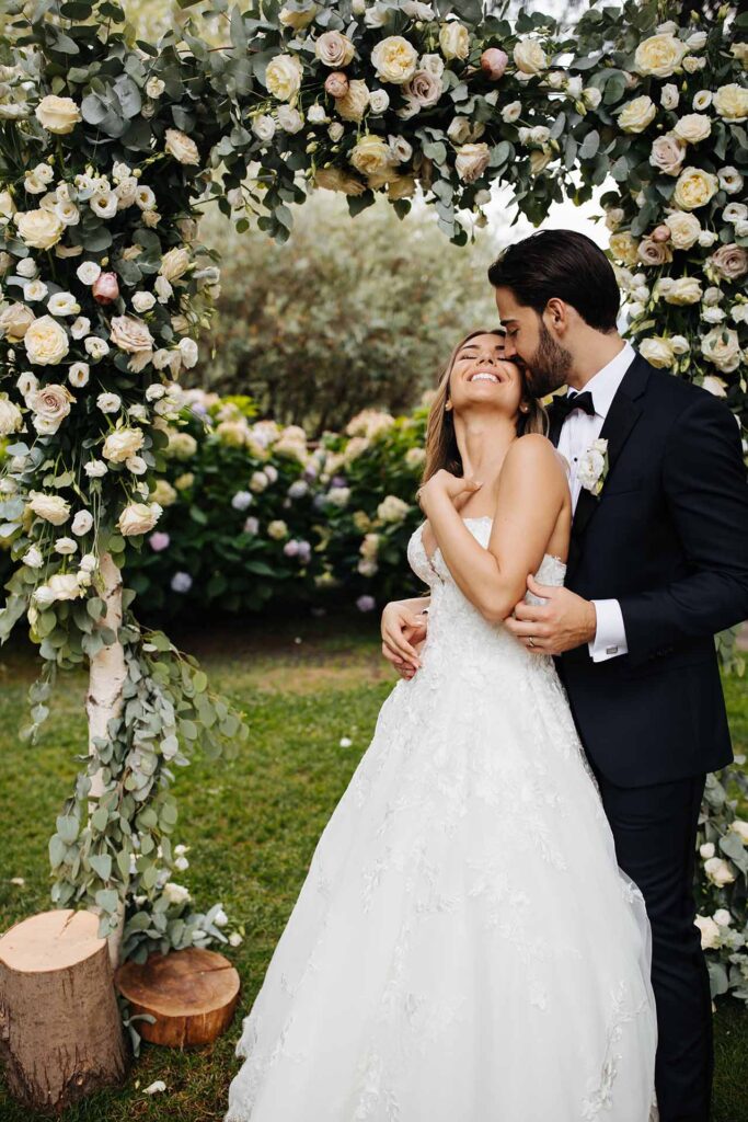 Bride and groom embracing under floral wedding arch at Castello di Rossino in Lake Como, Italy