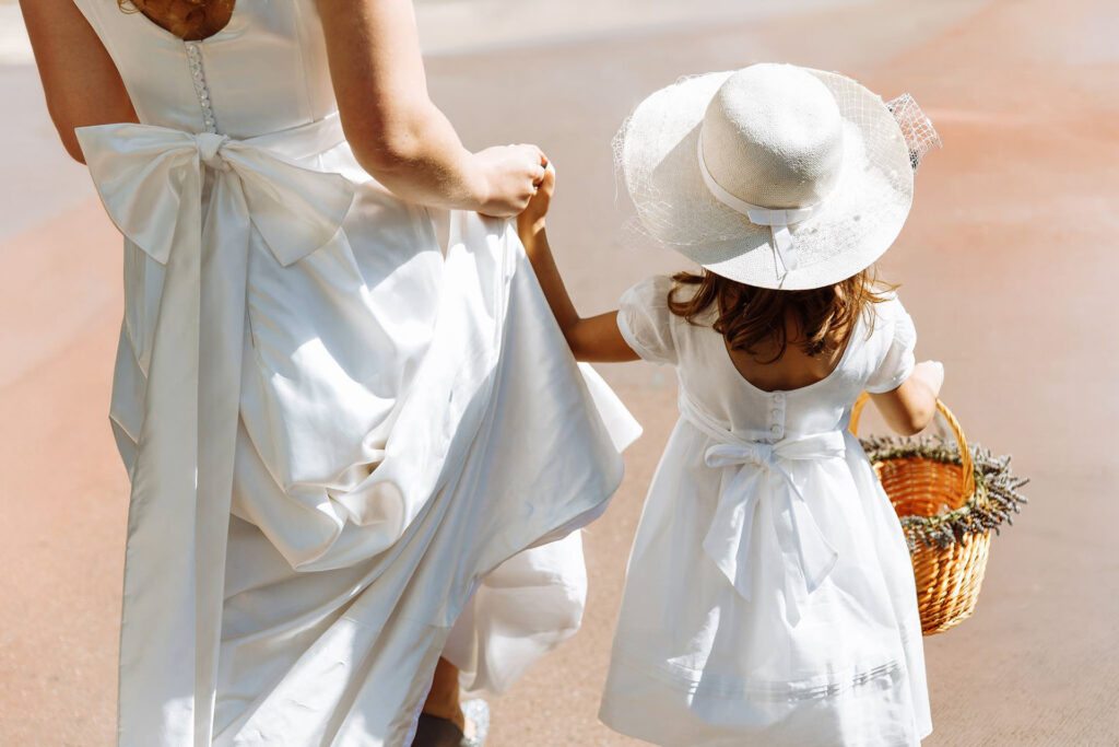 Elegant bride holding hands with a flower girl dressed in white carrying a basket during a luxury wedding in Italy