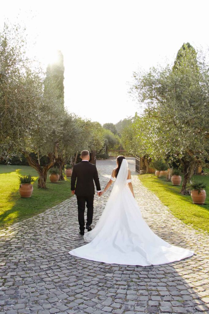 Bride and groom walking hand in hand at sunset through an olive garden during a luxury destination wedding in Rome, Italy