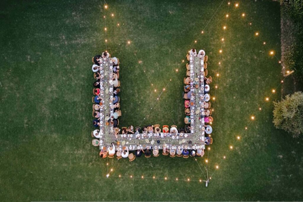 Aerial drone view of outdoor wedding reception with long banquet tables and romantic string lights