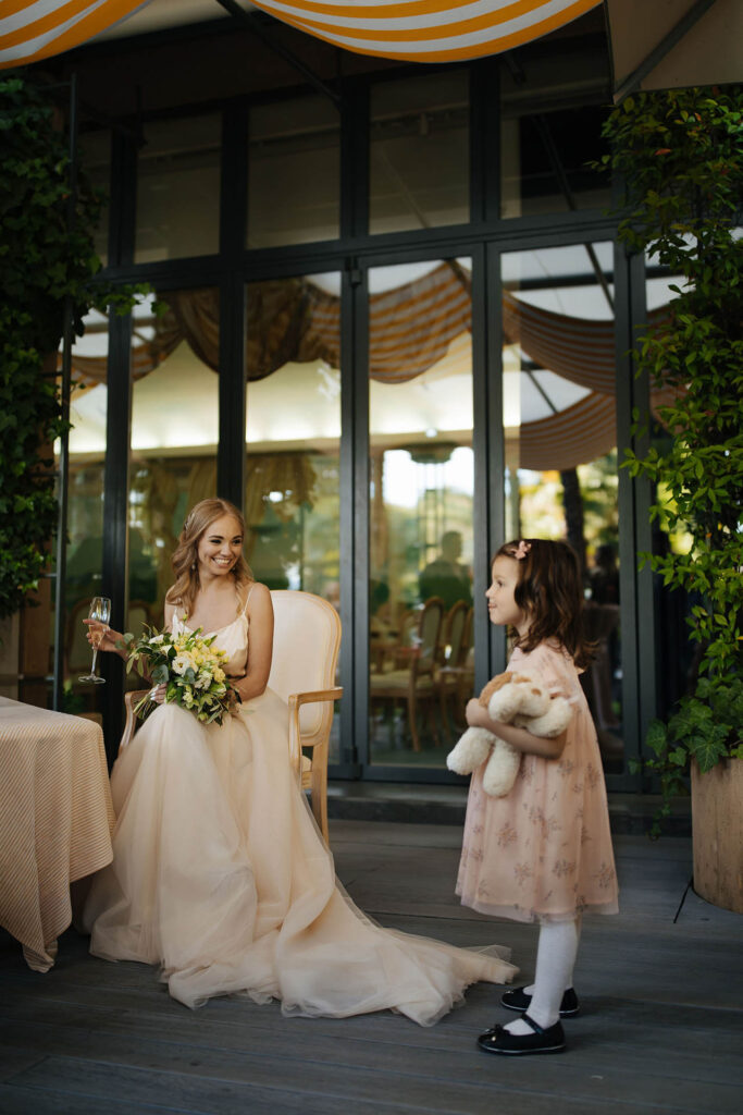 Bride sitting with bouquet at Grand Hotel Villa Castagnola in Lugano while young flower girl stands nearby during elegant wedding reception