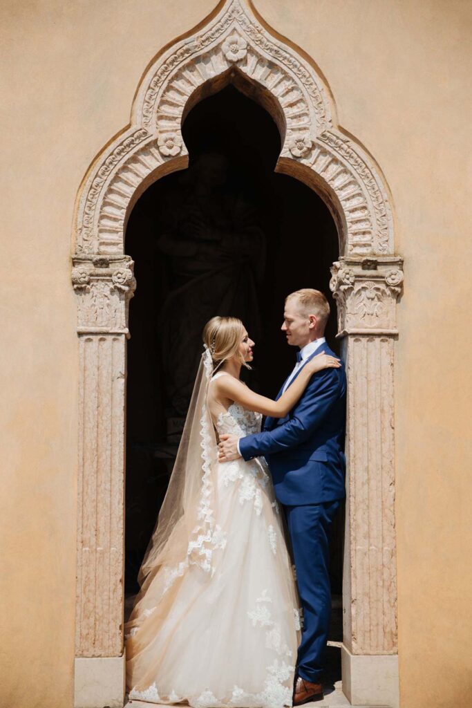 Bride and groom embracing under a historic stone archway at an Italian wedding venue