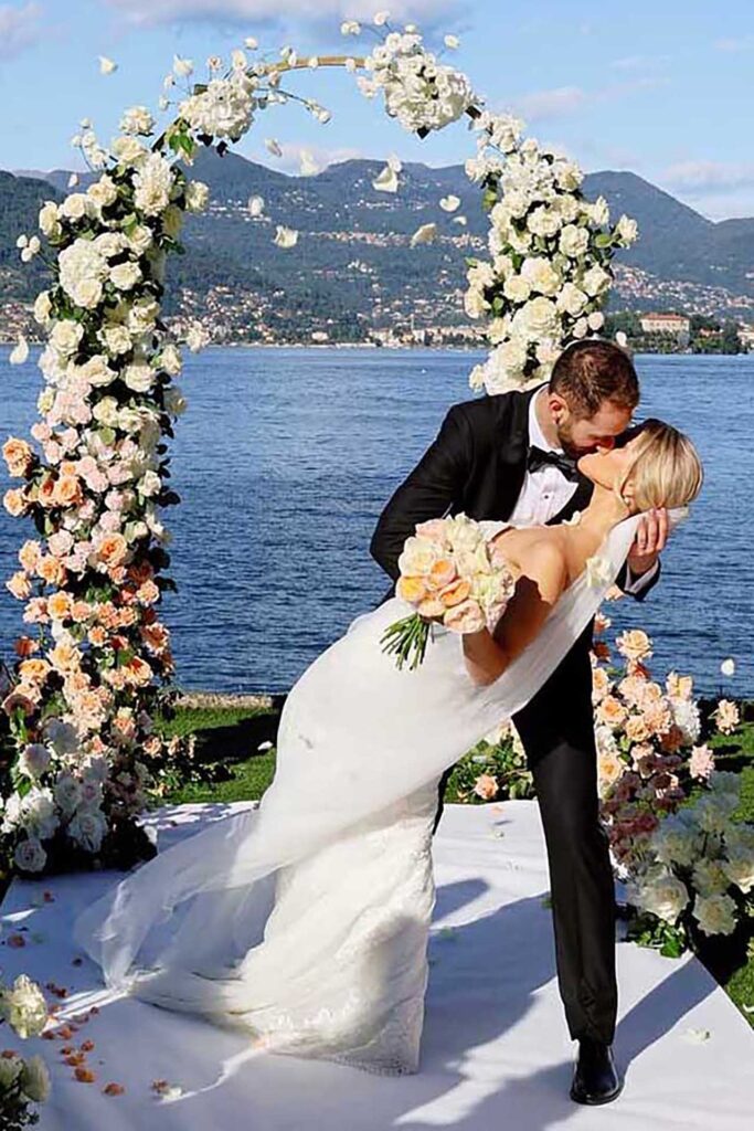 Bride and groom kissing under a floral arch during a luxury wedding ceremony overlooking Lake Maggiore, Italy