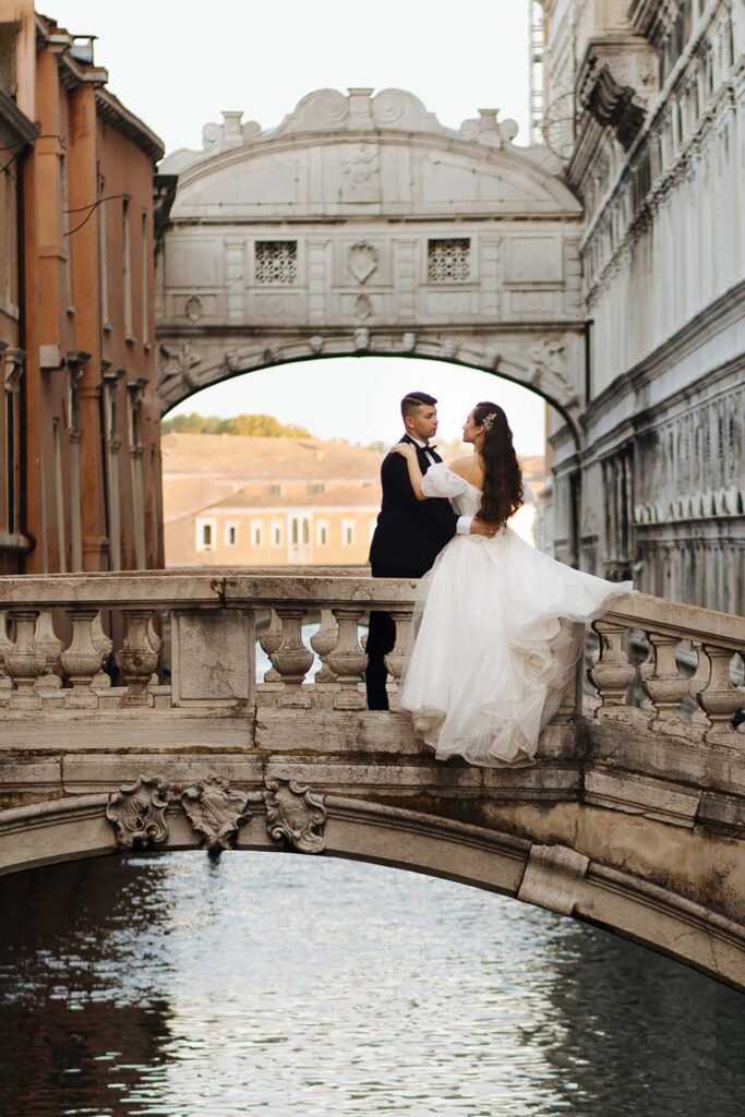Bride and groom embracing on a stone bridge near Ponte dei Sospiri in Venice during a romantic destination wedding in Italy