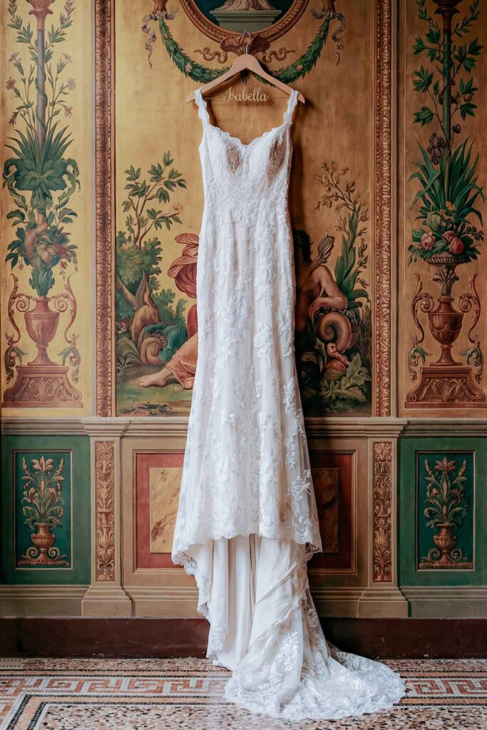 Luxury lace wedding dress hanging against an artistic Renaissance-style mural background in an editorial bridal setting