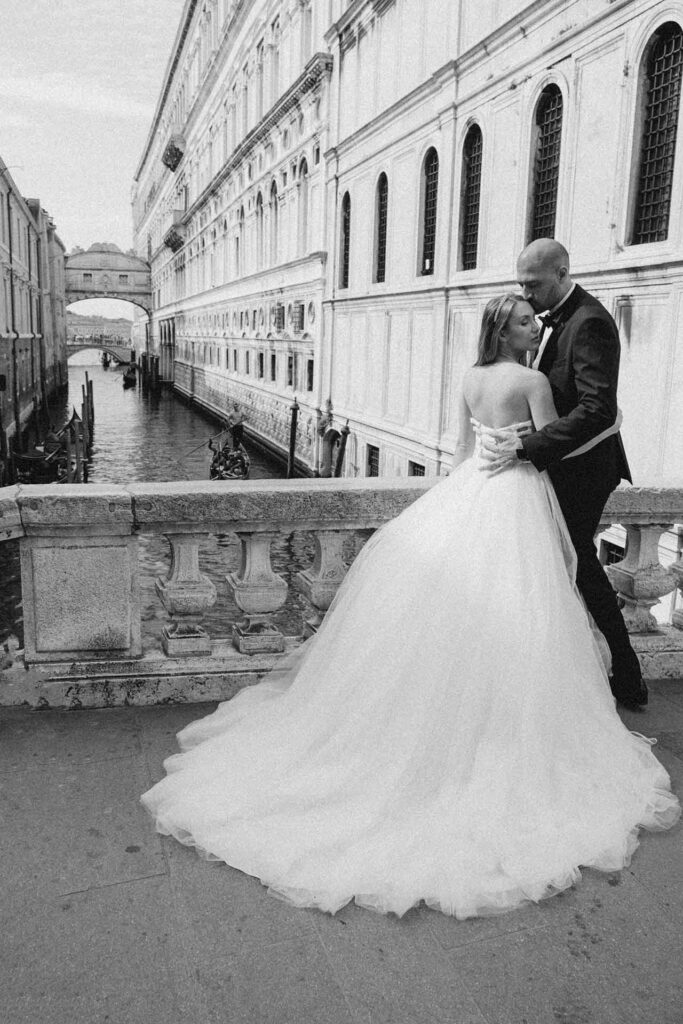 Bride and groom embracing on a historic bridge in Venice with the Bridge of Sighs and canal in the background