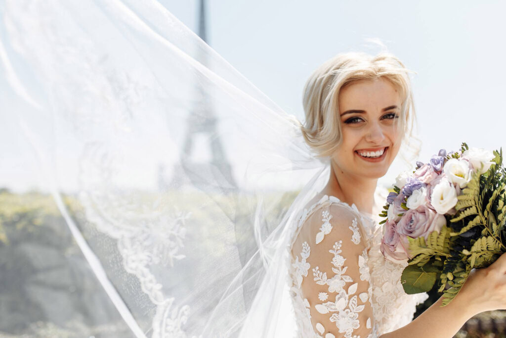 Smiling bride with veil and bouquet in front of the Eiffel Tower in Paris, France