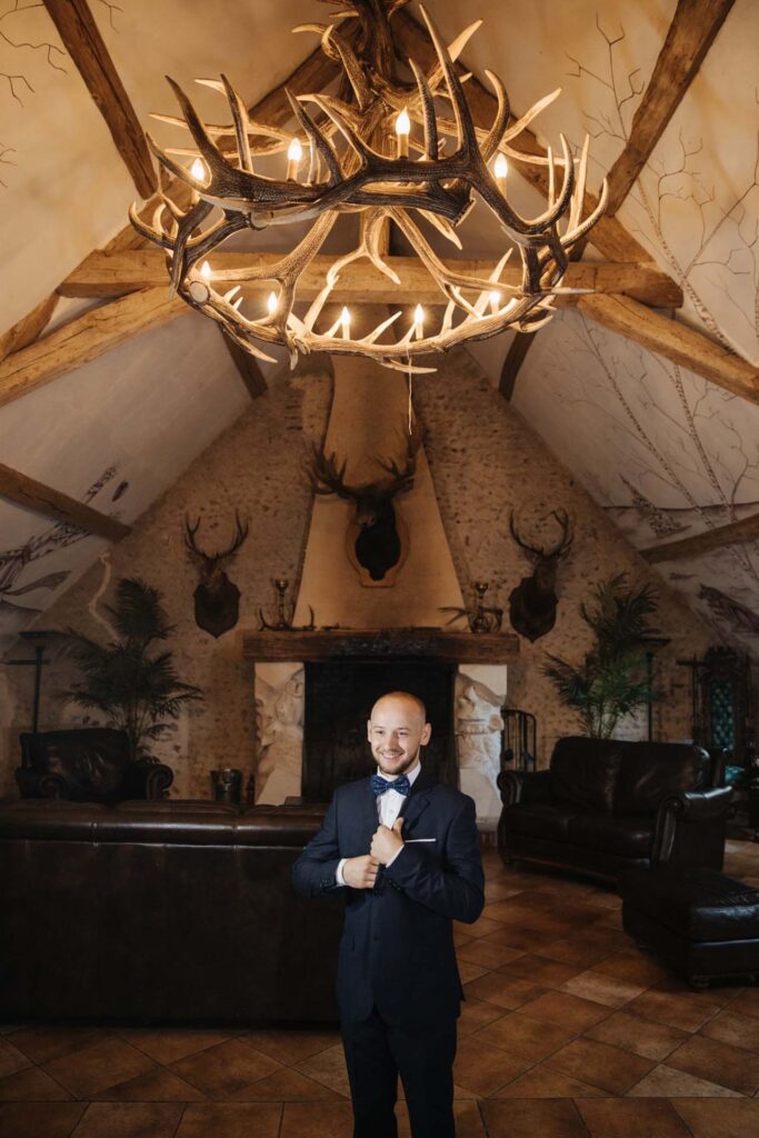 Elegant groom portrait inside a Paris château wedding venue with rustic chandelier and fireplace in France