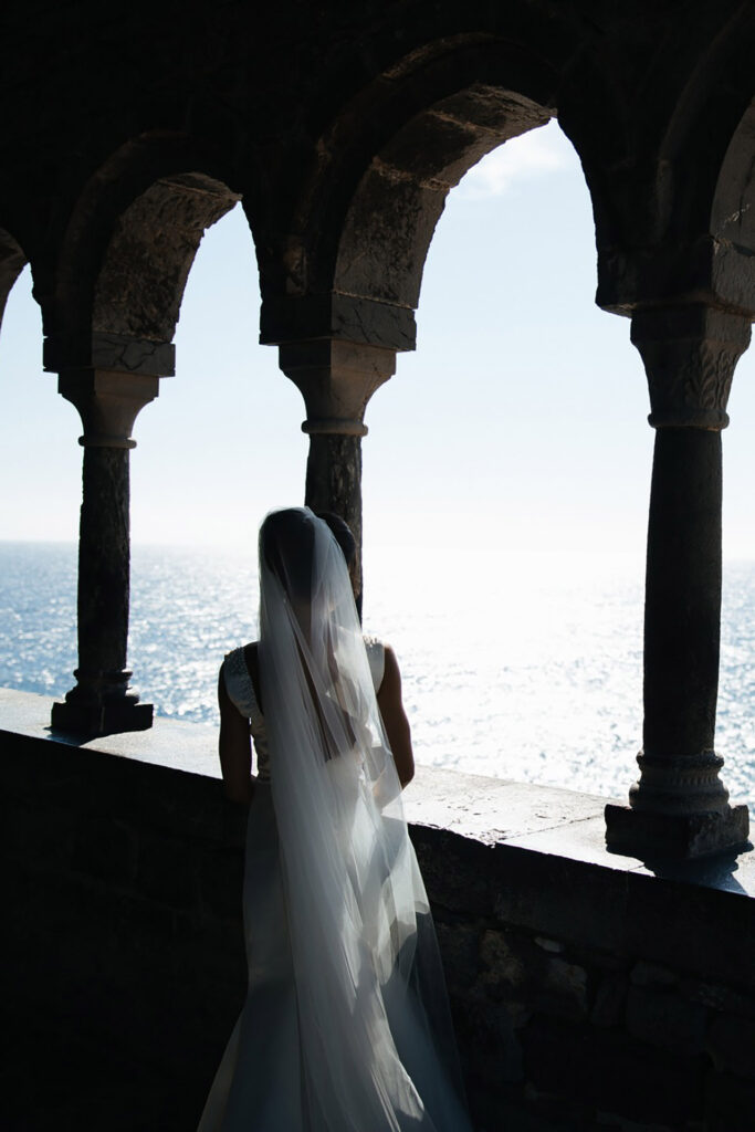 Bride standing under historic stone arches overlooking the sea in Portovenere, Liguria during a luxury destination wedding