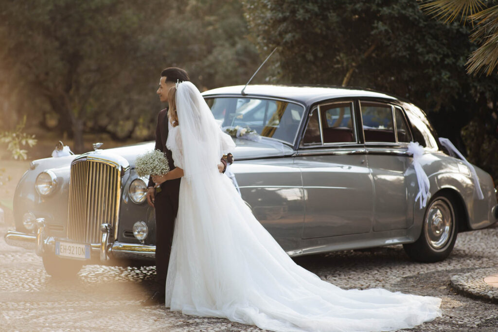 Bride and groom in Rome posing beside a vintage luxury wedding car in Italy during golden hour