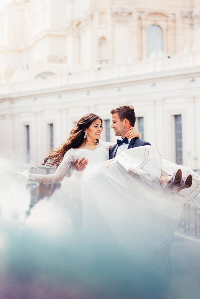 Romantic destination wedding portrait in Rome with groom carrying the bride in front of historic architecture