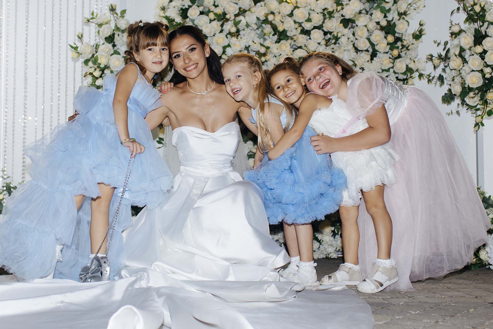 Bride with flower girls during wedding reception in Rome, Italy, in front of white floral backdrop
