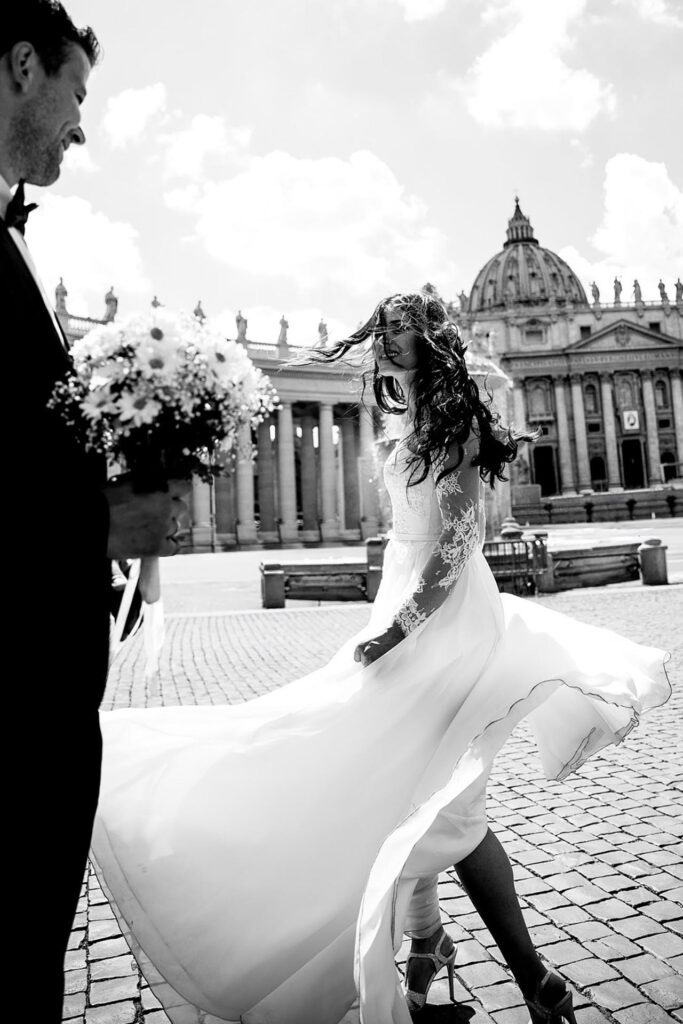 Bride in flowing wedding dress walking in St. Peter’s Square with St. Peter’s Basilica in the background in Rome