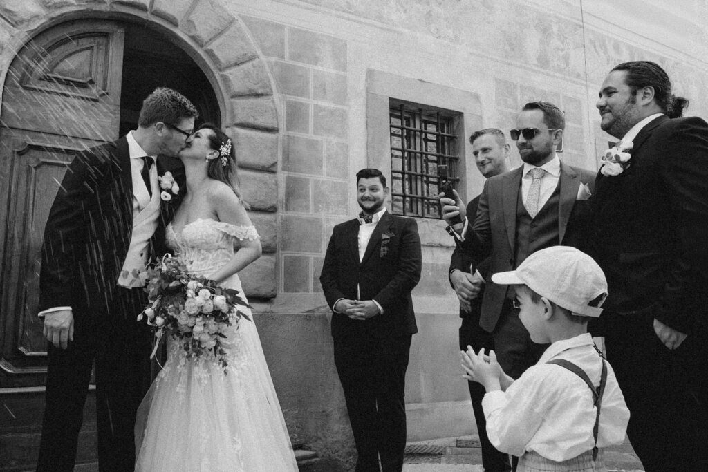 Bride and groom kissing during a wedding ceremony exit in Tuscany, Italy captured in timeless black and white photography