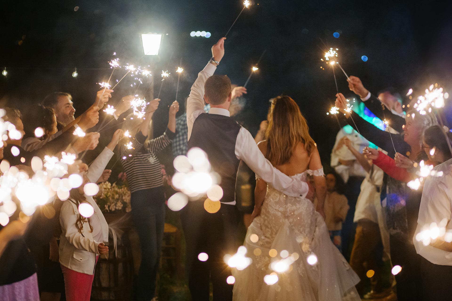 Bride and groom celebrating their wedding night with a sparkler exit in Tuscany, Italy surrounded by guests