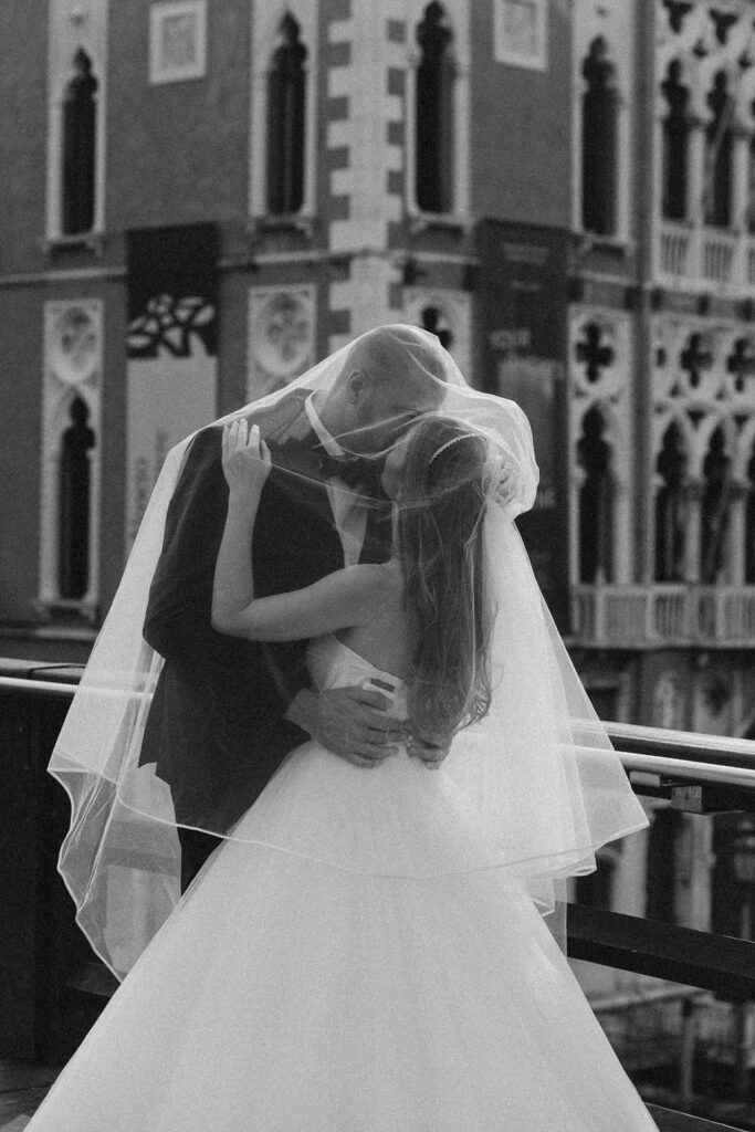 Bride and groom kissing under the veil on a balcony in Venice, Italy, black and white wedding portrait