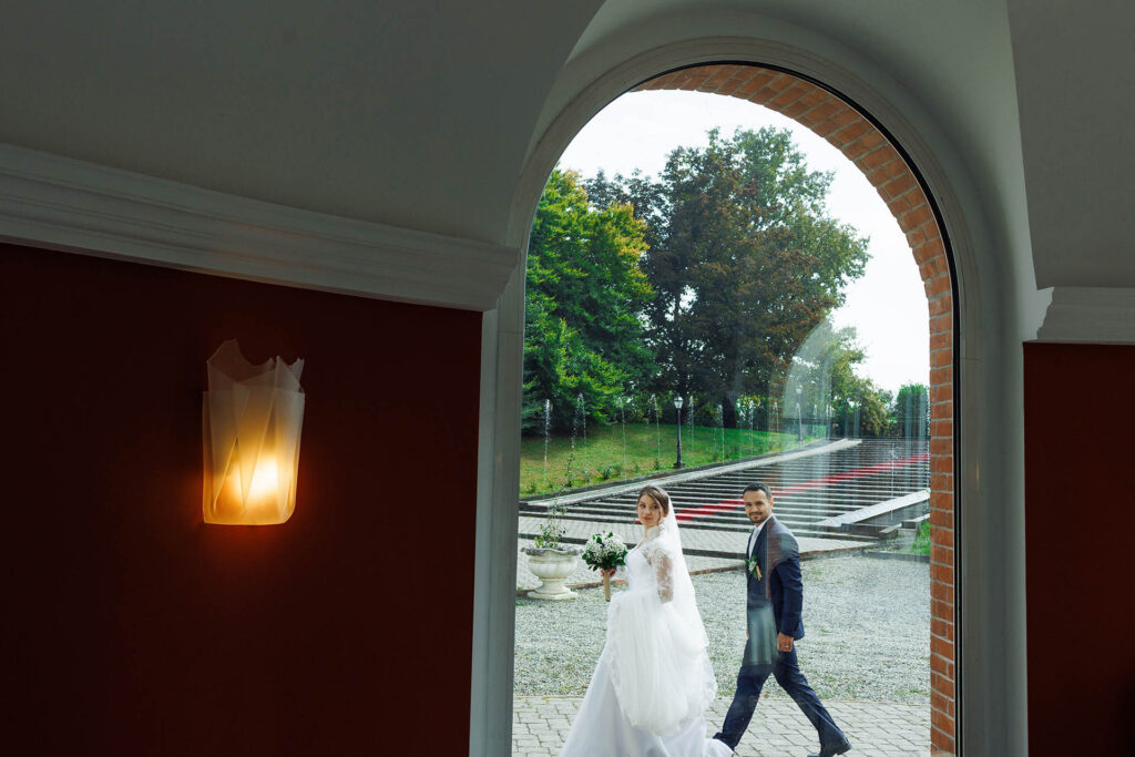 Bride and groom walking outside a historic villa in Alessandria, Italy, framed by an elegant arched doorway