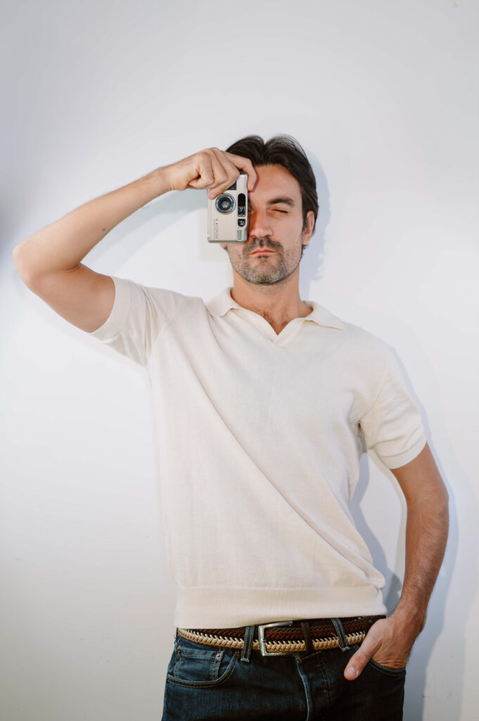 Professional photographer holding a compact camera to his eye against a clean white background