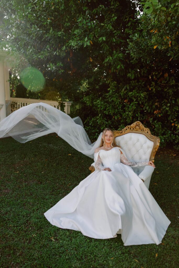 Bride seated on an ornate chair with her veil moving through the garden at a Rome wedding venue