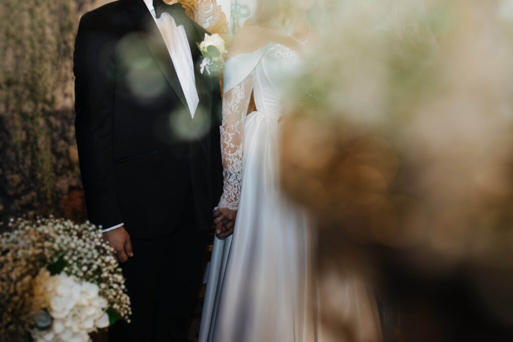 Close-up of bride and groom holding hands beside soft white wedding flowers