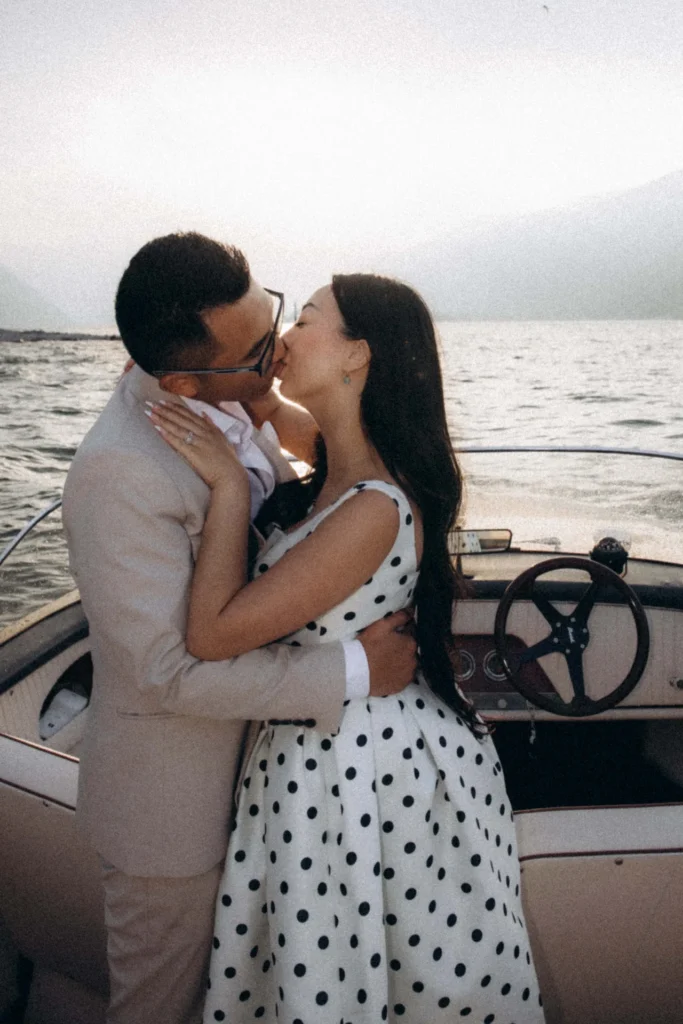 Couple kissing on a classic motorboat with Lake Como and shoreline behind them