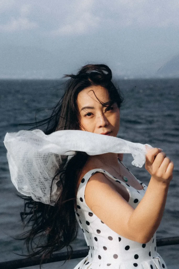 Woman turning toward the camera as wind lifts a white lace scarf by Lake Como