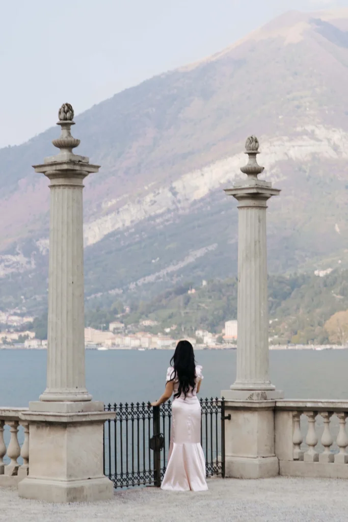 Woman seen from behind between two stone columns overlooking Lake Como and the mountains