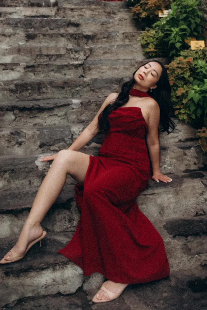 Woman in an elegant red dress seated on weathered stone steps in Varenna, Lake Como, Italy